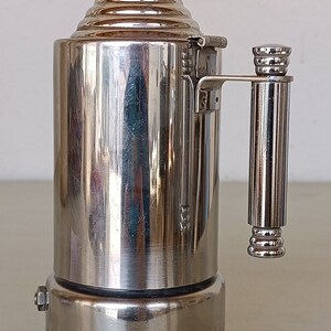 Peut inclure: Une cafeti&egrave;re vintage argent&eacute;e avec un corps cylindrique et un dessus conique. La poign&eacute;e et le dessus sont orn&eacute;s de motifs c&ocirc;tel&eacute;s. La base est marron fonc&eacute;. La cafeti&egrave;re est probablement en m&eacute;tal et pr&eacute;sente un design classique.