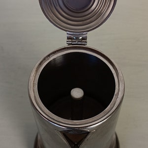 Peut inclure: Une cafeti&egrave;re en acier inoxydable avec le couvercle ouvert. Le corps cylindrique a un bec triangulaire et une base ronde. Le couvercle est articul&eacute; et poss&egrave;de une poign&eacute;e circulaire. L'int&eacute;rieur est sombre, avec un poteau central.