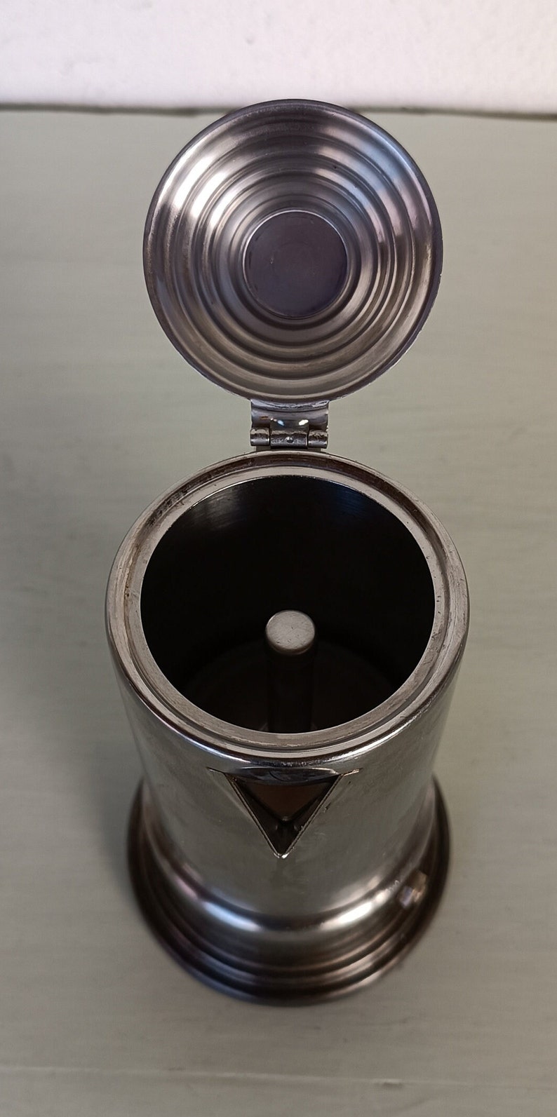 Peut inclure: Une cafeti&egrave;re en acier inoxydable avec le couvercle ouvert. Le corps cylindrique a un bec triangulaire et une base ronde. Le couvercle est articul&eacute; et poss&egrave;de une poign&eacute;e circulaire. L'int&eacute;rieur est sombre, avec un poteau central.