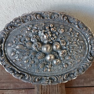 May include: Silver oval trinket box with an ornate design featuring a raised floral motif of fruit and leaves.