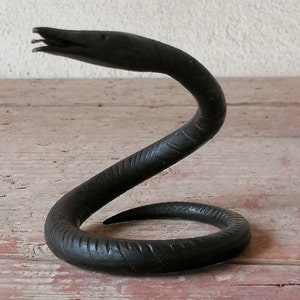 K&ouml;nnte beinhalten: Eine schwarze Schlangenskulptur aus Metall mit einem gewundenen K&ouml;rper und einem erhobenen Kopf. Die Schlange ist mit strukturierten Schuppen verziert.