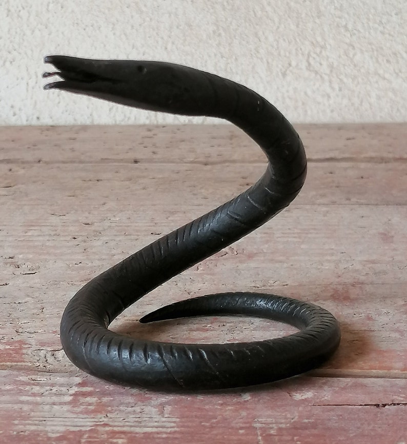K&ouml;nnte beinhalten: Eine schwarze Schlangenskulptur aus Metall mit einem gewundenen K&ouml;rper und einem erhobenen Kopf. Die Schlange ist mit strukturierten Schuppen verziert.