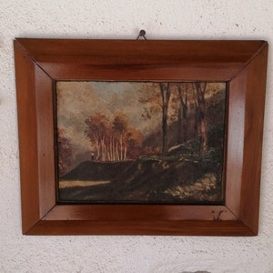 May include: A framed painting of a forest scene with trees and a hill in the background. The painting is in a brown wooden frame.
