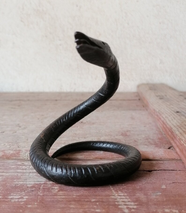 K&ouml;nnte beinhalten: Eine schwarze Schlangenskulptur aus Metall mit einem gewundenen K&ouml;rper und einem erhobenen Kopf. Die Schlange ist mit strukturierten Schuppen und einem leicht ge&ouml;ffneten Maul detailliert.
