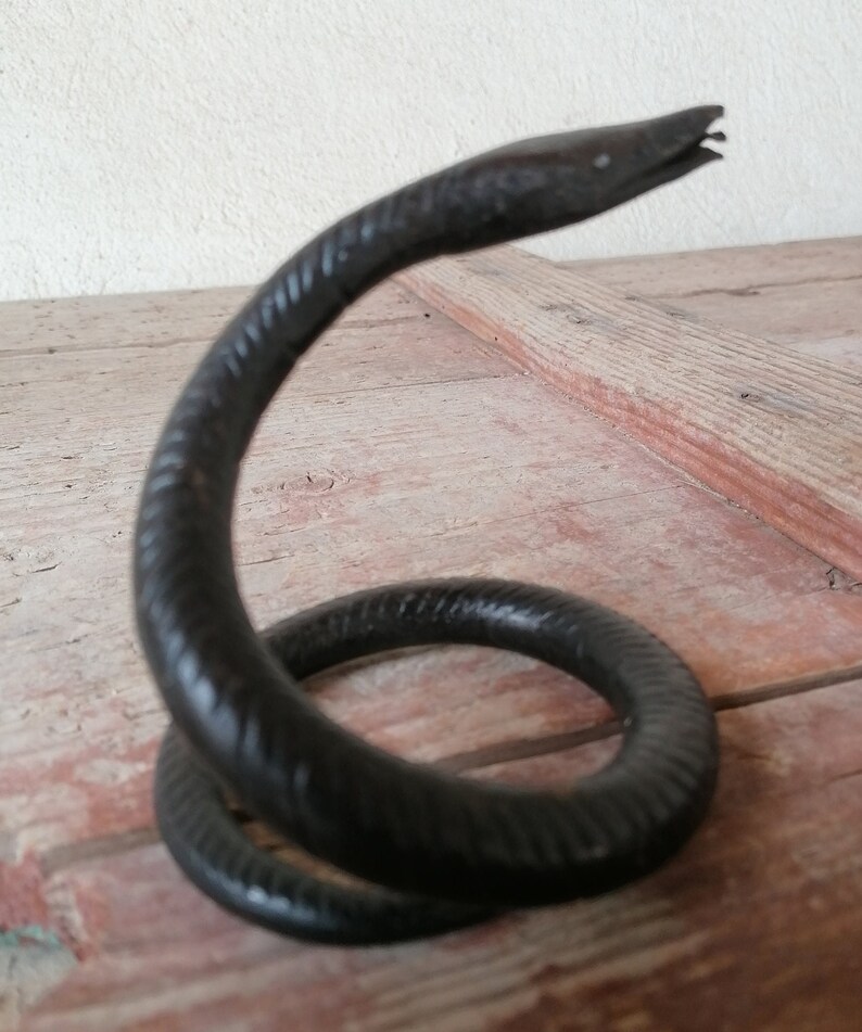 K&ouml;nnte beinhalten: Eine schwarze Schlangenskulptur aus Metall mit einem gewundenen K&ouml;rper und einem erhobenen Kopf. Die Schlange ist texturiert und hat ein realistisches Aussehen.