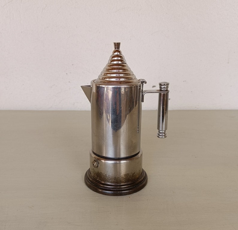 Peut inclure: Une cafeti&egrave;re italienne en acier inoxydable avec un couvercle conique et une poign&eacute;e. La cafeti&egrave;re a une base marron fonc&eacute; et un bec verseur. Le design est vintage et classique.
