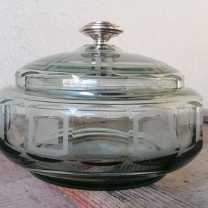 Könnte beinhalten: Eine gefrostete Glasdose mit einem silbernen Deckel und einem geometrischen Muster. Die Dose ist grün und hat eine runde Form.