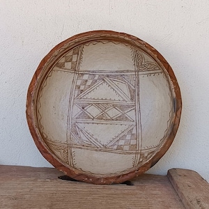 May include: A large, round, terracotta bowl with a white interior and a geometric design in brown. The bowl has a slightly raised rim.