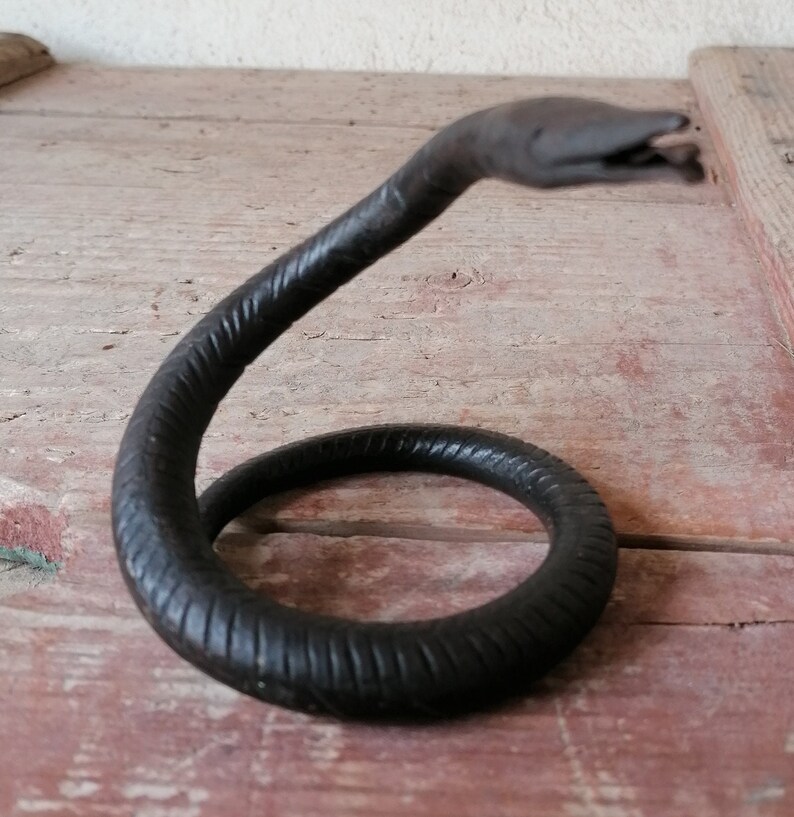 K&ouml;nnte beinhalten: Eine schwarze Schlangenskulptur aus Metall mit einem gewundenen K&ouml;rper und einem erhobenen Kopf. Die Skulptur hat eine strukturierte Oberfl&auml;che und besteht aus einem einzigen St&uuml;ck Metall.