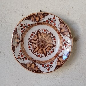 May include: A white ceramic plate with a brown and red floral design. The plate has a raised center with a floral pattern and a scalloped edge.