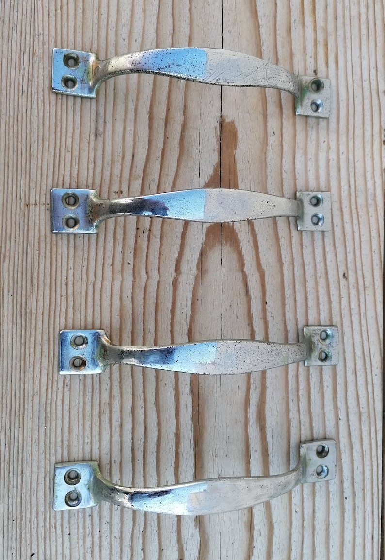 May include: Four silver cabinet door handles with a brushed finish. The handles are in a row on a wooden surface.