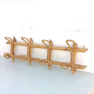 Könnte beinhalten: Ein natürlicher Wand-Kleiderhaken aus Bambus mit fünf Haken. Der Kleiderhaken hat ein rechteckiges Design mit vertikalen und horizontalen Bambusteilen und gebogenen Haken. Das Bambus hat eine hellbraune Farbe.