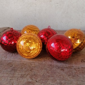 Può includere: Sei addobbi natalizi lucidi in rosso e oro. Gli addobbi sono rotondi e hanno un design sfaccettato. Sono disposti su una superficie di legno.