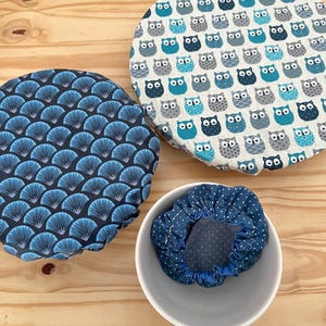 Peut inclure: Trois couvercles de bols réutilisables avec différents motifs. L'un présente un imprimé de hiboux bleus et blancs, un autre un motif de ventilateur bleu et le troisième un motif à pois bleus. Les couvercles sont sur une surface en bois.