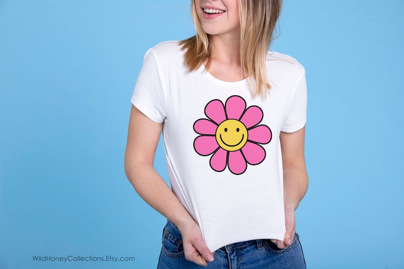May include: White t-shirt with a pink flower graphic featuring a yellow smiley face.