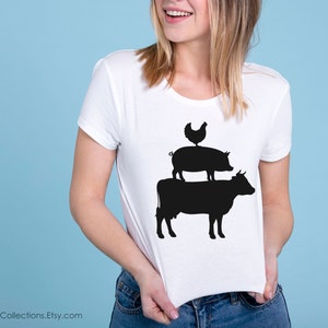 May include: A white t-shirt with a black silhouette of a cow, pig, and chicken stacked on top of each other.