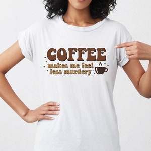 May include: White t-shirt with brown text that reads "Coffee makes me feel less murdery."  The text is in a retro font style with a coffee cup graphic.