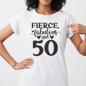 Pu&ograve; includere: T-shirt bianca con la scritta nera "FIERCE, fabulous and 50". La parola "fabulous" &egrave; in un carattere script, e il numero 50 &egrave; in grassetto, senza grazie. Due piccoli cuori neri sono tra "fabulous" e "50".