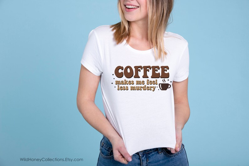 May include: White t-shirt with brown text that reads "COFFEE makes me feel less murdery."  A small brown coffee cup icon is next to the text.