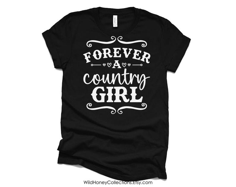 Puede incluir: Una camiseta negra de manga corta con el texto impreso en blanco FOREVER A country GIRL, decorada con remolinos y peque&ntilde;os iconos de corazones centrados en el pecho de la prenda, que cuenta con un cuello redondo est&aacute;ndar.