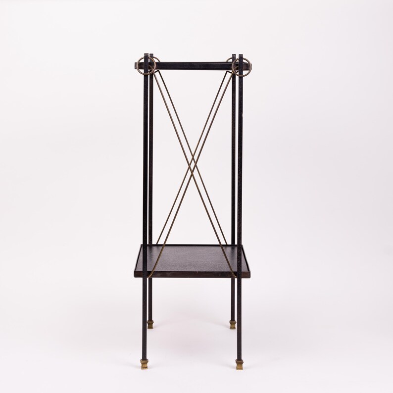 May include: A black metal plant stand with a rectangular shelf and four legs. The stand features brass accents on the legs and decorative elements at the top. The stand has a minimalist design.