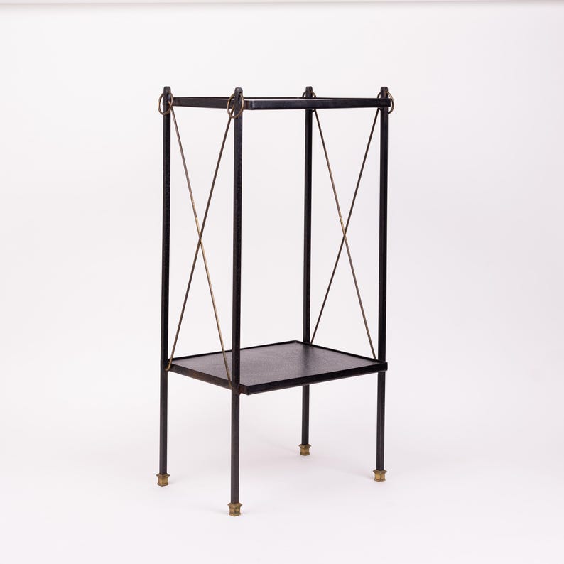 Peut inclure: Une table d'appoint en métal noir avec un plateau et une étagère carrés. La table a quatre pieds avec des accents de couleur laiton en bas. Le cadre comporte des supports croisés et des anneaux décoratifs de couleur laiton.