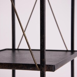 May include: A black metal shelf with three tiers. The shelves are square and the supports are made of thin, dark metal. Diagonal brass-colored metal rods provide additional support. The shelf is against a white background.