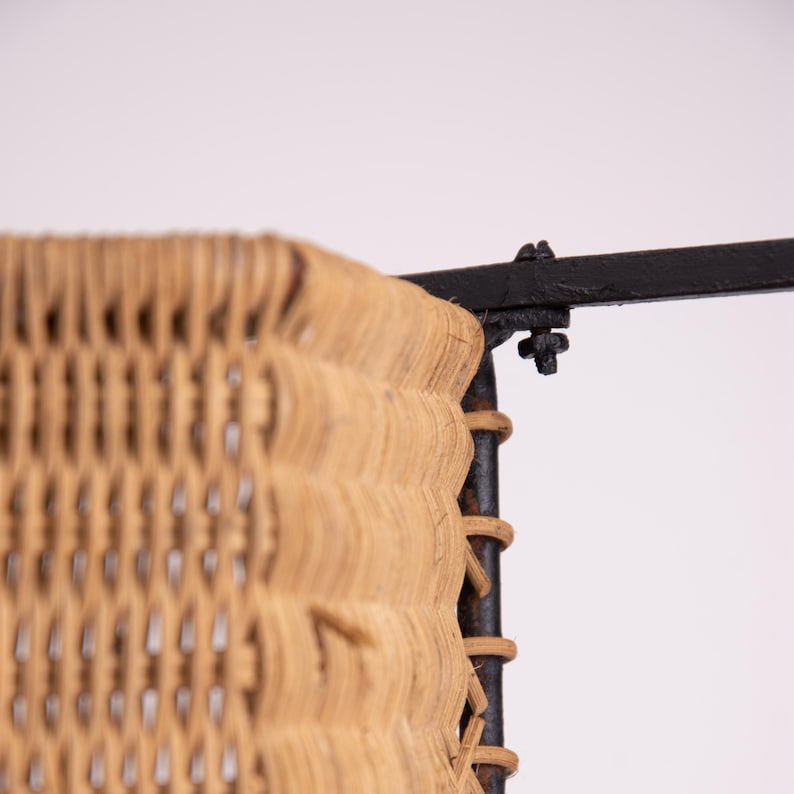 May include: Close-up of a woven wicker panel with a black metal frame. The wicker is a light tan color, and the weave is visible. The metal frame is attached with bolts. The design is likely for a chair or other furniture.