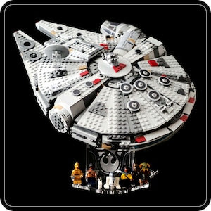 Puede incluir: Una nave espacial Lego Millennium Falcon blanca y gris con detalles rojos y dorados. La nave espacial está en un soporte de exhibición transparente con un símbolo de la Alianza Rebelde. Hay varias minifiguras de Lego en el soporte, incluyendo Han Solo, Chewbacca, la princesa Leia, Luke Skywalker y R2-D2.