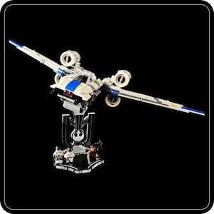 Op de afbeelding: Een model X-wing Starfighter, een wit en blauw ruimteschip, wordt getoond op een transparante standaard met de tekst "X-WING STARFIGHTER" en miniatuurfiguren. Het model heeft gedetailleerde vleugels en motoren, tegen een zwarte achtergrond.
