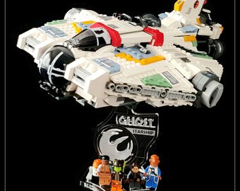 May include: A white Lego Star Wars Ghost starship with a clear acrylic display stand. The stand features the words "Ghost Starship" and the Rebel Alliance symbol. Five Lego minifigures are standing in front of the stand.