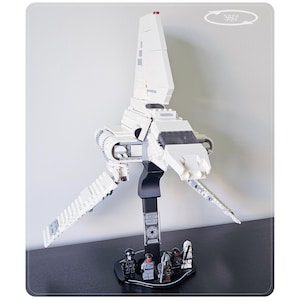 May include: A white plastic brick-built Lambda-class shuttle model mounted on a black display stand. The stand features a plaque labelled Lambda Class Shuttle 75302 and five small character figurines standing at the base of the support column.