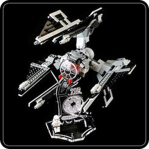 May include: A black and gray TIE Defender Lego set with a clear display stand. The stand has the words "The Defender" printed on it. The TIE Defender is in flight mode with the wings extended.