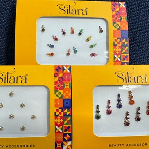 May include: Three packages of Silara beauty accessories. Each package contains a variety of rhinestones in different colors and shapes. The packages are yellow with a colorful pattern.