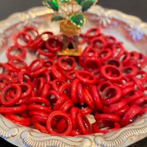 May include: A silver tray with a small green plant figurine in the center. The tray is filled with red rings.