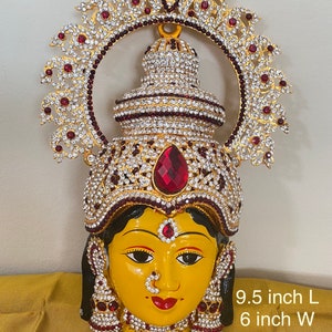 May include: A gold and red decorative face mask with rhinestones and a crown. The mask is 9.5 inches long and 6 inches wide.