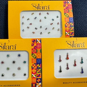 May include: Three yellow boxes with the brand name "Silara" printed on them. Each box contains a sheet of colorful, decorative, self-adhesive gems for the face or body. The boxes are labeled "Beauty Accessories".