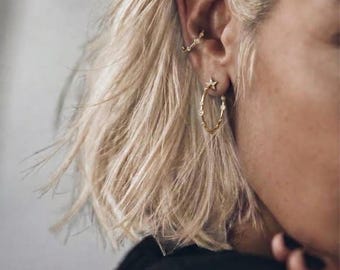 May include: A gold hoop earring featuring a small star charm and embedded clear stones, paired with a matching gold ear cuff adorned with small clear stones. Both pieces are worn on the ear, showcasing a delicate metallic design with sparkling accents.