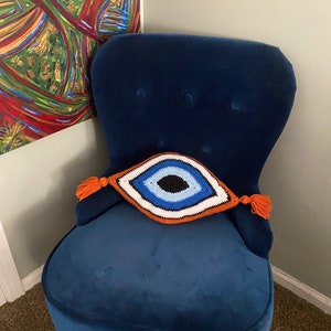 以下が含まれることがあります： オレンジ色のタッセルが付いた、青いベルベットの肘掛け椅子と、クロシェで編まれた邪悪な目のクッション。クッションは青、白、黒です。