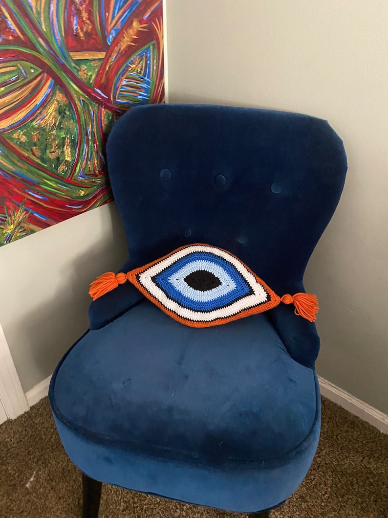 以下が含まれることがあります： オレンジ色のタッセルが付いた、青いベルベットの肘掛け椅子と、クロシェで編まれた邪悪な目のクッション。クッションは青、白、黒です。