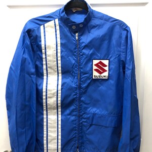 May include: A blue vintage Suzuki racing jacket with white racing stripes down the sleeves and a red and white Suzuki logo on the right chest.