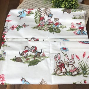 May include: Two white fabric panels with a whimsical woodland print. The design features cartoon animals, including bunnies, squirrels, and birds, along with mushrooms, flowers, and leaves. The color palette includes red, blue, green, and brown.