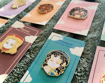 Puede incluir: Una colección de pines de esmalte con retratos de personajes estilizados sobre tarjetas rectangulares. Cada tarjeta muestra el nombre de un personaje, como Marius y Pandora, con gráficos de nubes y una URL. Los pines son metálicos con esmalte.