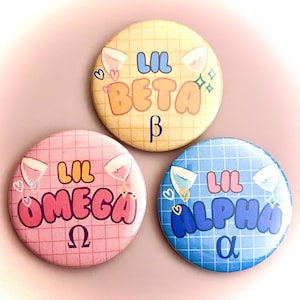 May include: Three circular badges with the text "Lil Beta", "Lil Omega", and "Lil Alpha" in bubble letters. Each badge has a different colour background: yellow, pink, and blue. Each badge has a grid pattern and a cartoon design.