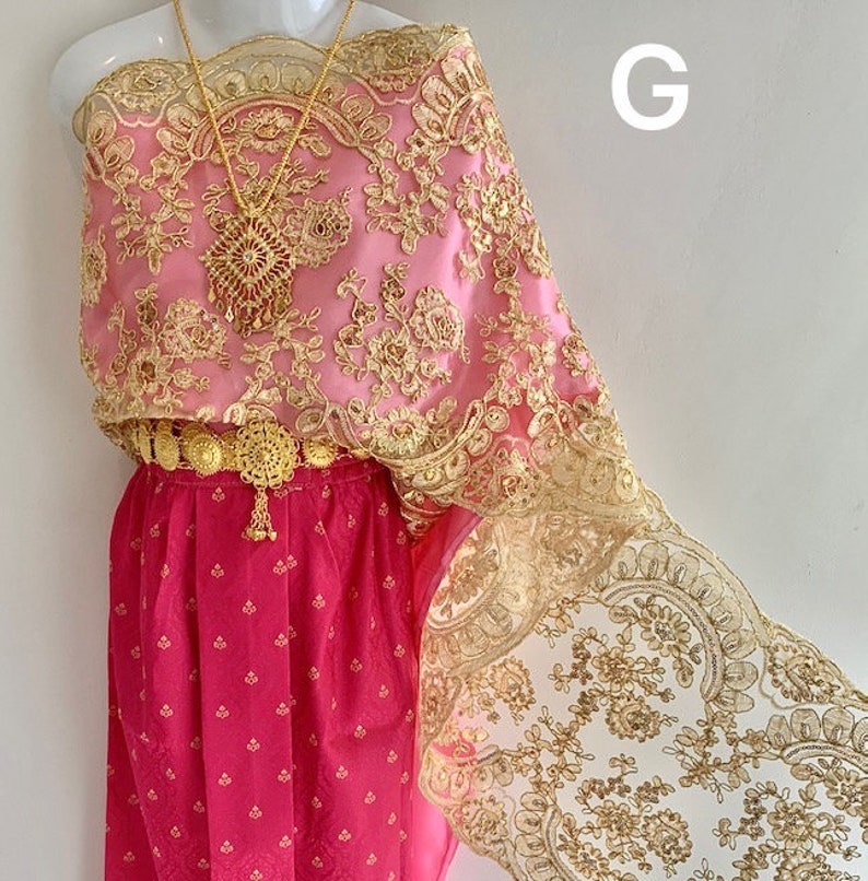 May include: A pink and gold traditional Thai dress with intricate lace detailing. The dress features a gold belt and a gold necklace.