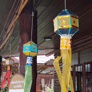 May include: Two blue and gold paper lanterns hanging from a wooden ceiling. The lanterns have a decorative fringe and are decorated with gold and white patterns. The lanterns are hanging in a covered outdoor area.