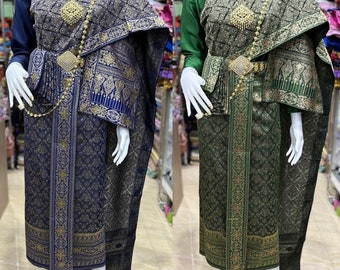 May include: Two traditional Thai outfits, one in dark blue and gold, the other in green and gold, with intricate patterns and gold accents. Both outfits feature a long skirt, a top with a high collar, and a shawl.