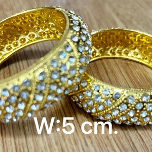 May include: Two gold bangles with clear rhinestones. The bangles are 5 cm wide.