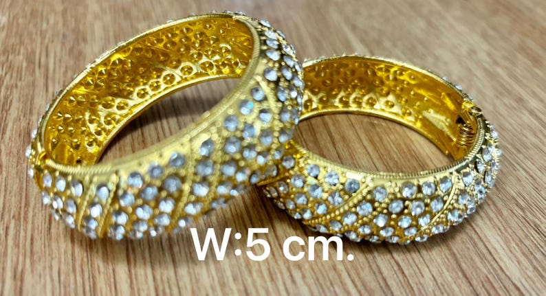 May include: Two gold bangles with clear rhinestones. The bangles are 5 cm wide.
