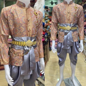 May include: A traditional Thai outfit with a long-sleeved, gold and pink patterned shirt and matching pants. The outfit includes a gold belt with a decorative buckle and a gray sash.